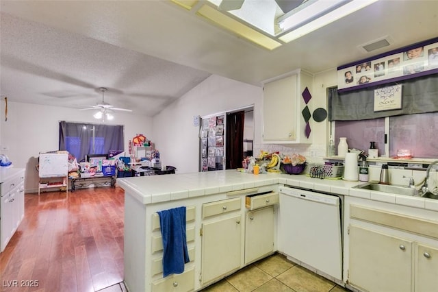 kitchen featuring a peninsula, visible vents, white dishwasher, and tile counters