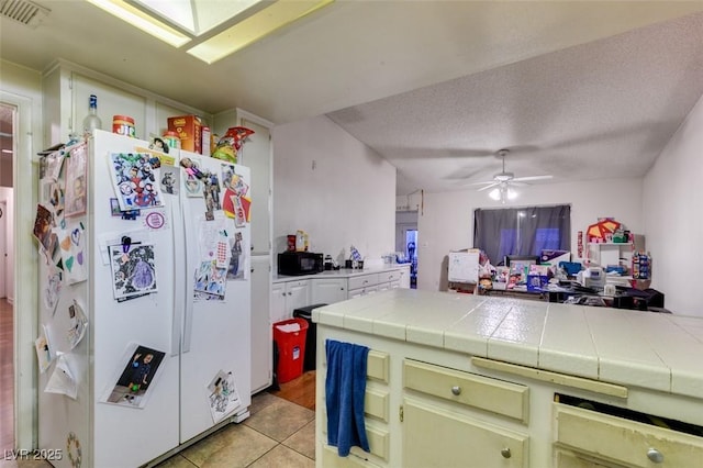 kitchen featuring light tile patterned floors, tile counters, visible vents, white fridge with ice dispenser, and black microwave