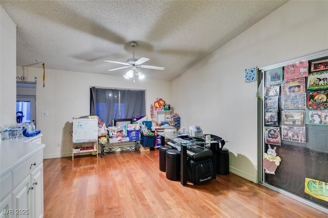 playroom with light wood finished floors, baseboards, a ceiling fan, and a textured ceiling