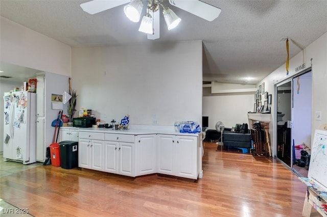 kitchen featuring black microwave, white cabinets, light countertops, light wood-type flooring, and freestanding refrigerator