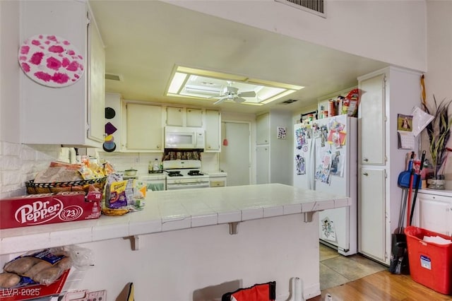 kitchen with ceiling fan, a peninsula, white appliances, tile counters, and tasteful backsplash