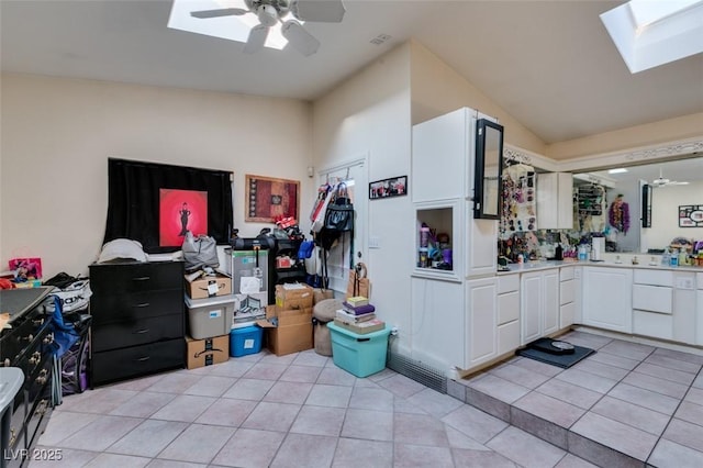 kitchen featuring light tile patterned floors, white cabinetry, a ceiling fan, light countertops, and lofted ceiling with skylight