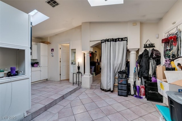 interior space featuring a skylight, decorative columns, light tile patterned floors, visible vents, and white cabinetry