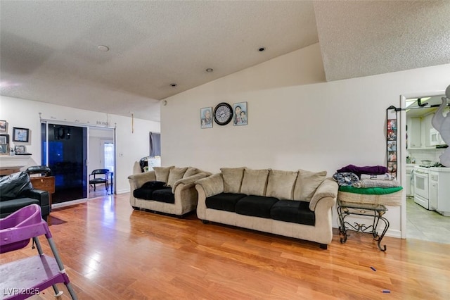 living room featuring lofted ceiling, light wood-style floors, and a textured ceiling