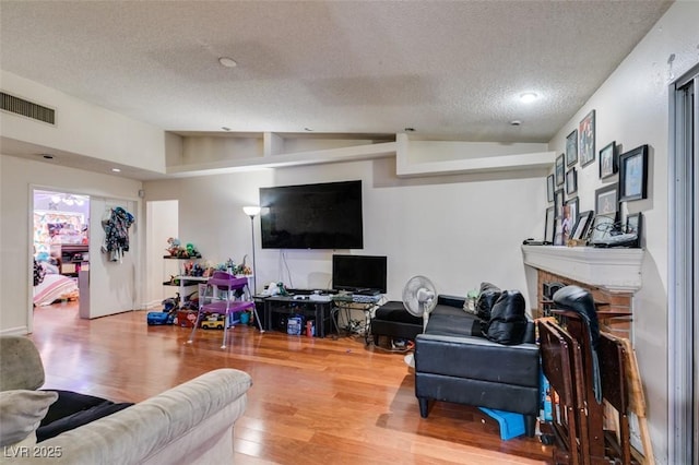 living room featuring lofted ceiling, a textured ceiling, a fireplace, wood finished floors, and visible vents