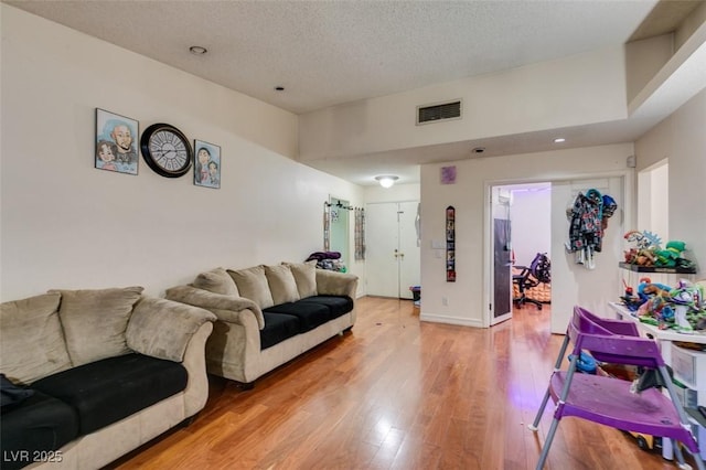 living room featuring light wood-type flooring, visible vents, a textured ceiling, and baseboards