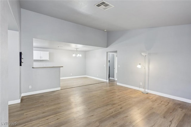 spare room featuring baseboards, visible vents, vaulted ceiling, light wood-type flooring, and a chandelier