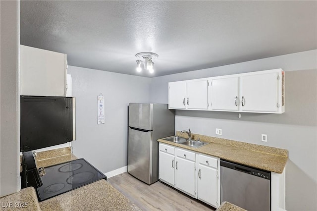 kitchen with light countertops, appliances with stainless steel finishes, white cabinets, a sink, and light wood-type flooring