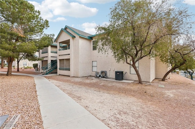 view of side of property featuring stairs, central AC, and stucco siding