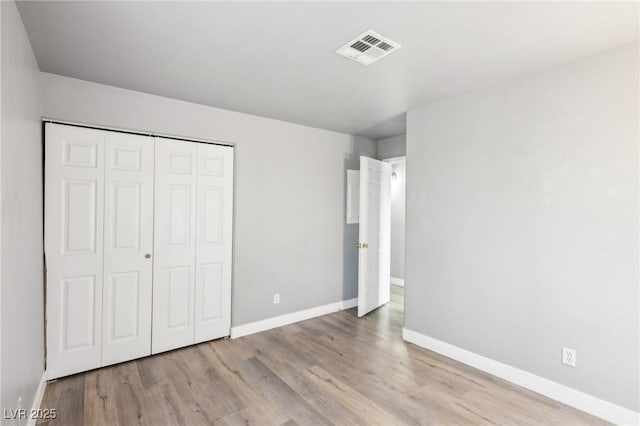 unfurnished bedroom featuring a closet, wood finished floors, visible vents, and baseboards