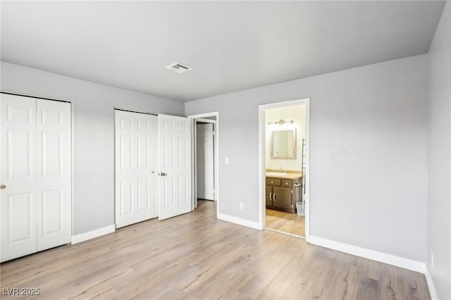 unfurnished bedroom with a sink, light wood-type flooring, baseboards, and multiple closets