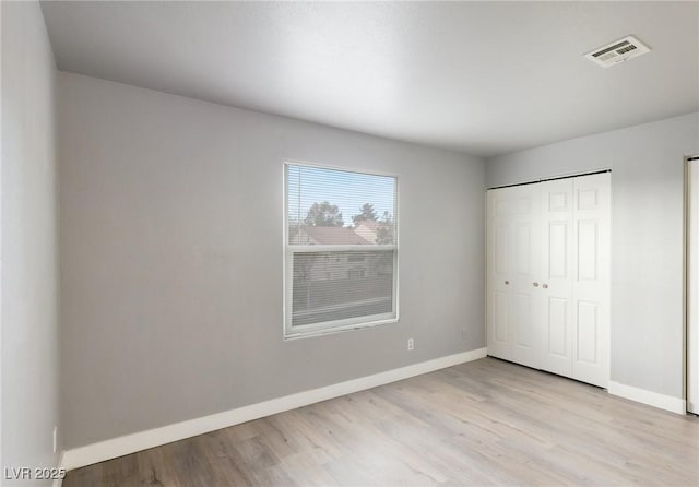 unfurnished bedroom with a closet, visible vents, baseboards, and wood finished floors