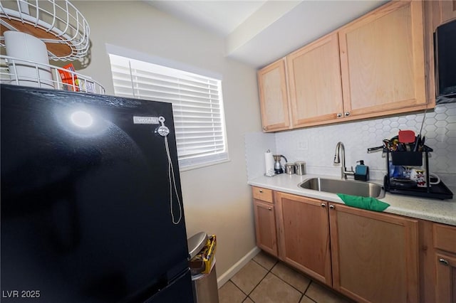 kitchen featuring light countertops, backsplash, freestanding refrigerator, light tile patterned flooring, and a sink