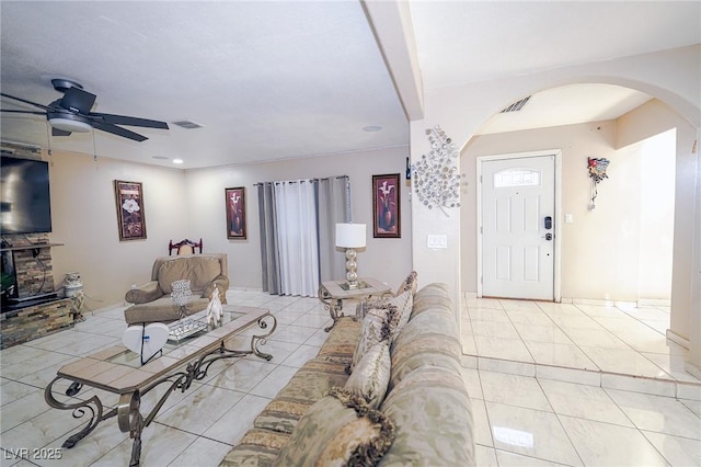 living room with light tile patterned floors, visible vents, arched walkways, and ceiling fan