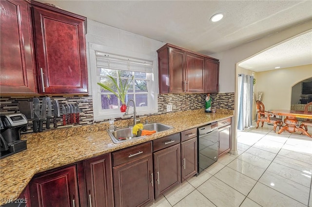 kitchen featuring decorative backsplash, dishwasher, light stone countertops, dark brown cabinets, and a sink