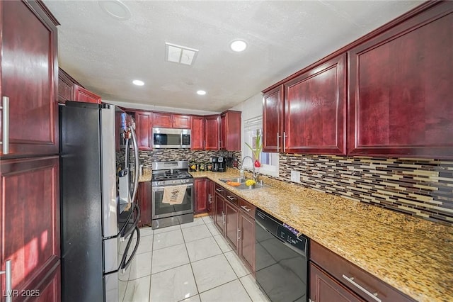 kitchen featuring reddish brown cabinets, light stone counters, light tile patterned floors, stainless steel appliances, and a sink