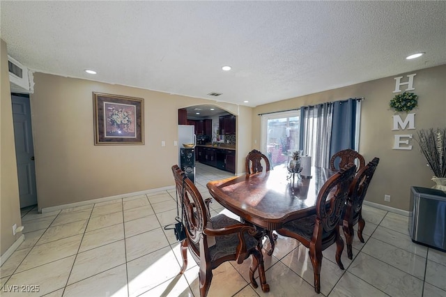 dining area with arched walkways, a textured ceiling, baseboards, and light tile patterned floors