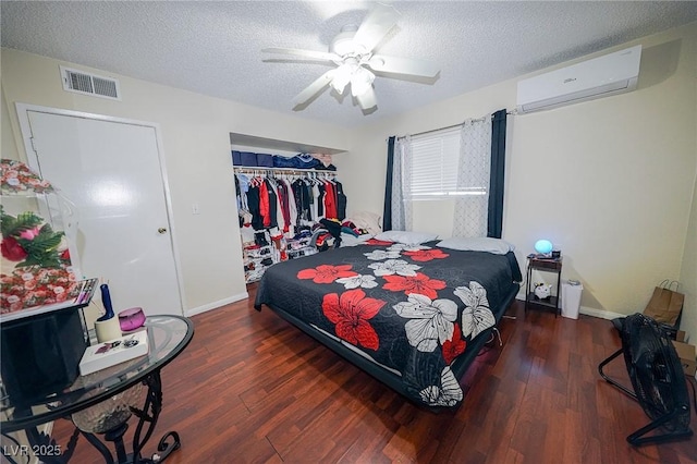 bedroom featuring a wall mounted air conditioner, visible vents, a textured ceiling, and wood finished floors