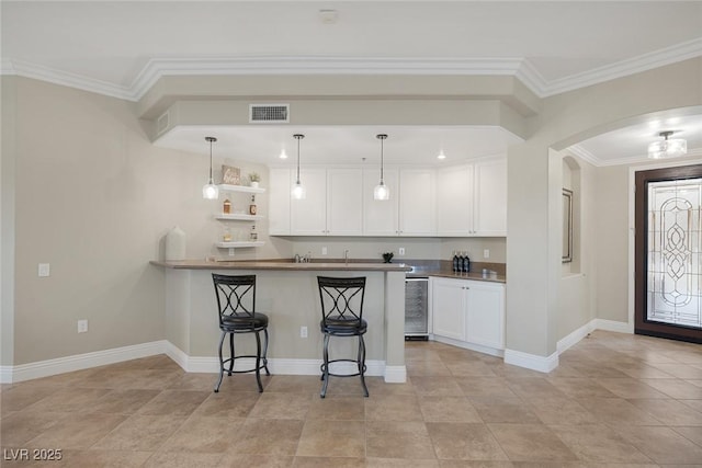 kitchen featuring arched walkways, wine cooler, a breakfast bar area, visible vents, and white cabinetry