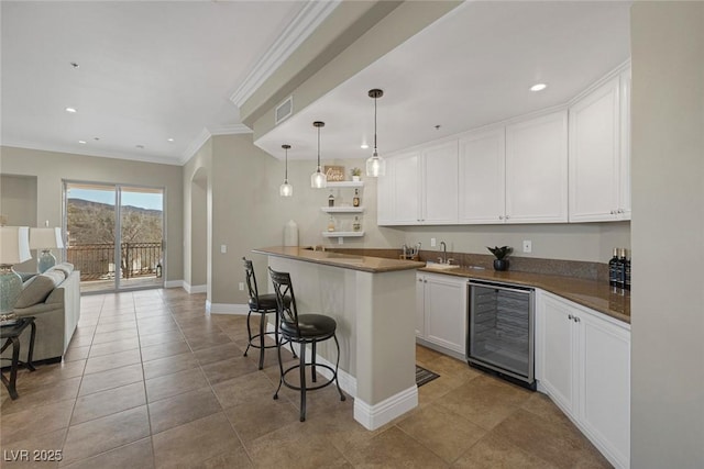 kitchen with wine cooler, open floor plan, crown molding, a kitchen bar, and white cabinetry