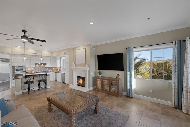 living area featuring a ceiling fan, a warm lit fireplace, crown molding, and baseboards