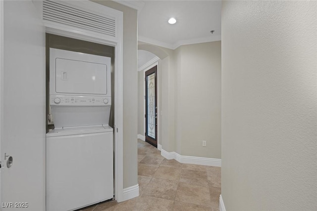 laundry area featuring arched walkways, stacked washer and dryer, laundry area, baseboards, and ornamental molding