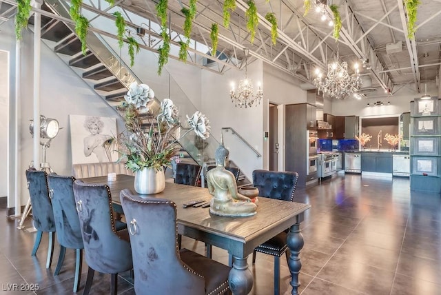 dining area with a towering ceiling, stairs, a chandelier, and dark tile patterned flooring