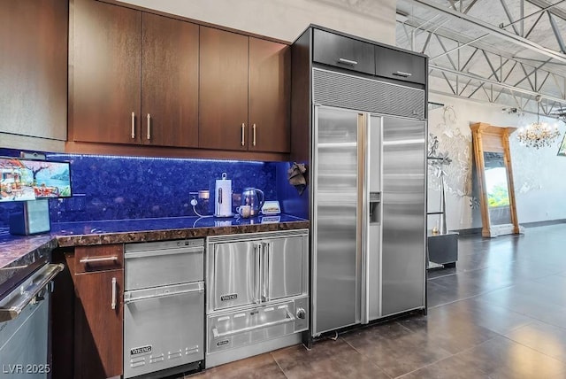 kitchen featuring dark stone counters, dark brown cabinets, a warming drawer, tasteful backsplash, and stainless steel built in refrigerator