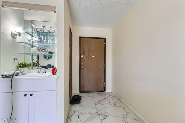 doorway to outside with marble finish floor, a sink, a textured ceiling, and baseboards