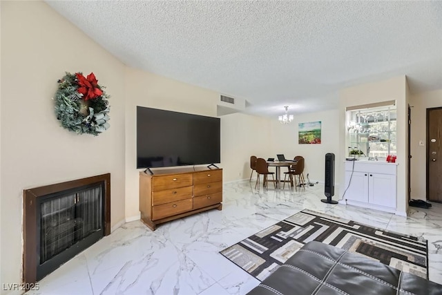 living room featuring visible vents, marble finish floor, an inviting chandelier, a textured ceiling, and a fireplace