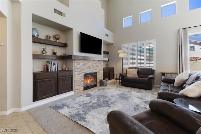 living area with built in features, visible vents, light tile patterned flooring, a stone fireplace, and baseboards