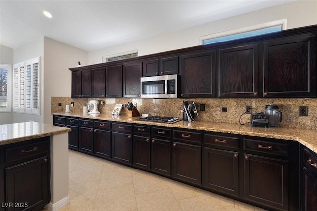 kitchen with light tile patterned floors, appliances with stainless steel finishes, backsplash, and light stone countertops