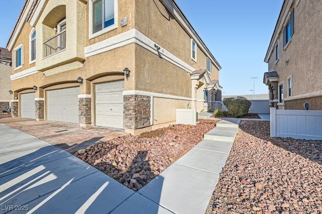 view of side of home featuring an attached garage, fence, stone siding, and stucco siding