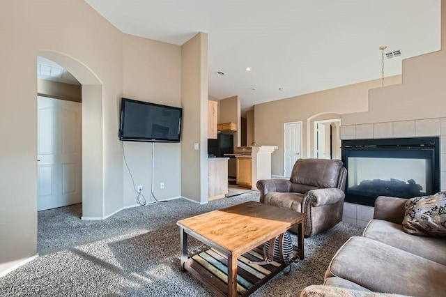 carpeted living area with a tiled fireplace, visible vents, arched walkways, and baseboards