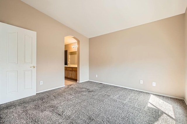 unfurnished bedroom featuring baseboards, ensuite bath, lofted ceiling, arched walkways, and light colored carpet