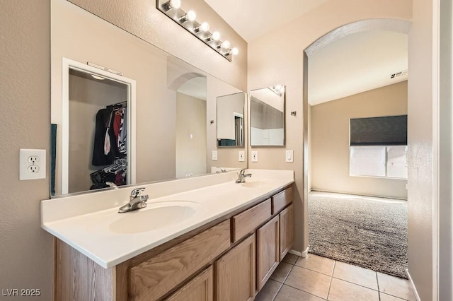 bathroom with tile patterned flooring, vaulted ceiling, double vanity, and a sink