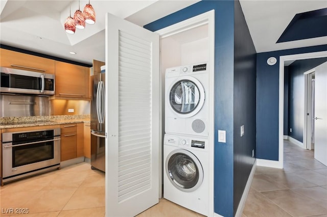 kitchen with light tile patterned floors, stainless steel appliances, stacked washer / drying machine, and light stone countertops