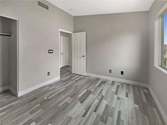 unfurnished bedroom featuring lofted ceiling, light wood-style floors, visible vents, and baseboards