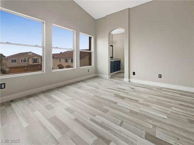 empty room featuring arched walkways, light wood-type flooring, and baseboards