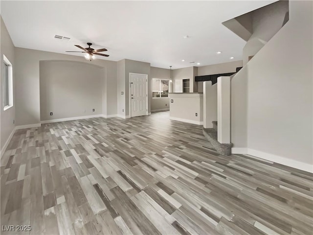 unfurnished living room featuring light wood-style flooring, stairway, visible vents, and baseboards