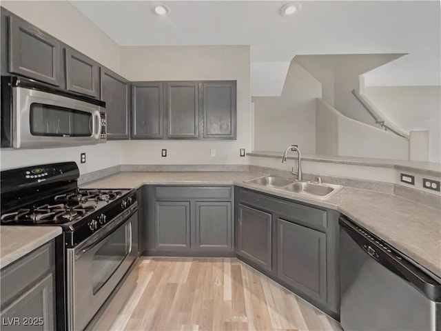 kitchen with gray cabinetry, stainless steel appliances, a sink, light countertops, and light wood finished floors