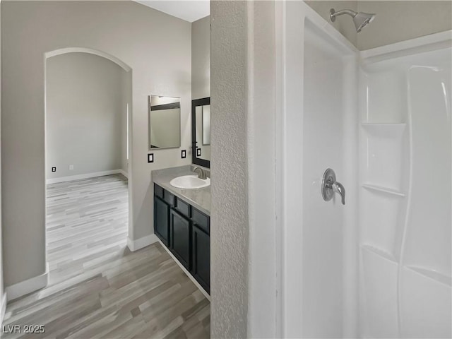 bathroom featuring baseboards, a shower, wood finished floors, and vanity