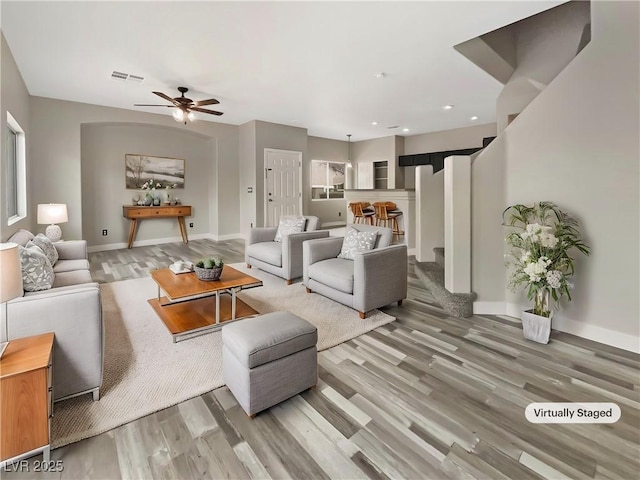 living area featuring a ceiling fan, baseboards, visible vents, and wood finished floors