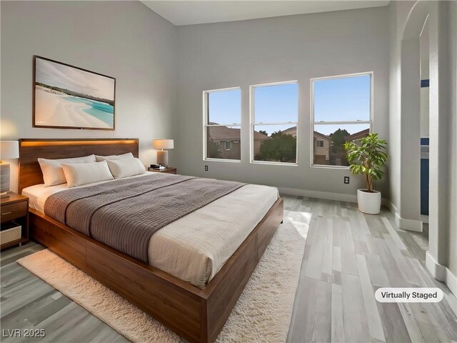 bedroom featuring arched walkways, wood finished floors, and baseboards