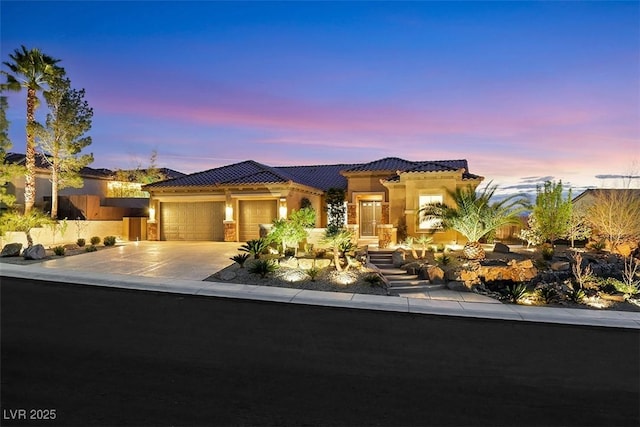 mediterranean / spanish-style house with a garage, concrete driveway, stucco siding, and a tiled roof