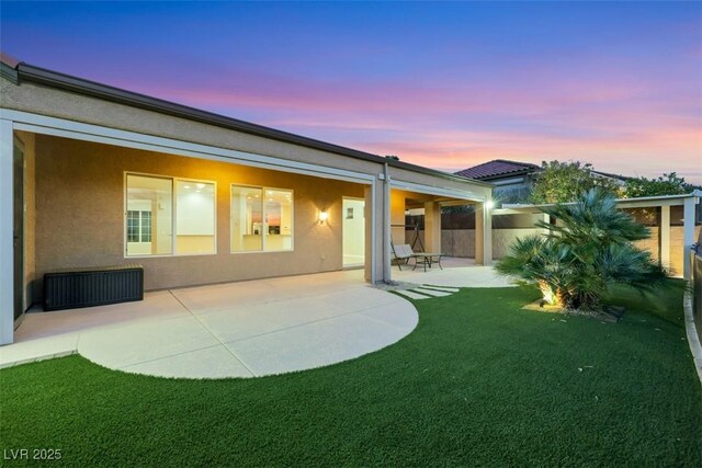 back of property at dusk with a patio area and stucco siding