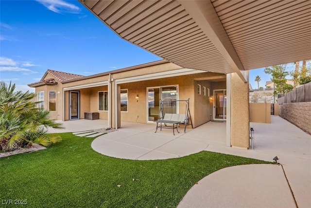 rear view of house with fence, a tile roof, stucco siding, a lawn, and a patio area