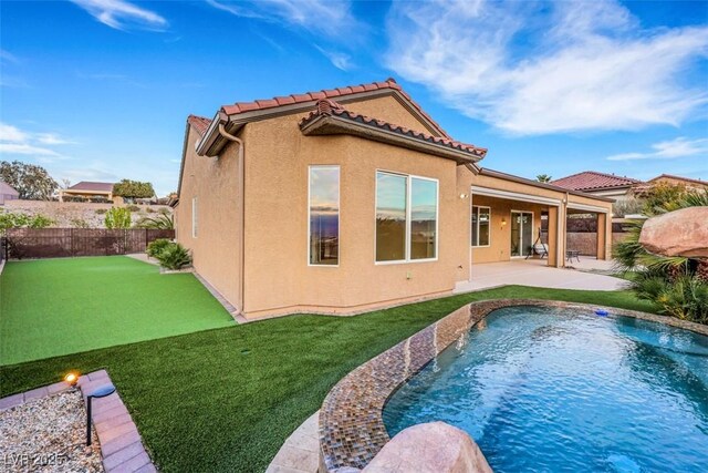 back of house with stucco siding, a lawn, a tile roof, a patio, and a fenced backyard