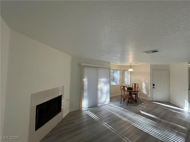 5044 S Rainbow Blvd Unit 106, Las Vegas, NV 89118 - living room featuring a textured ceiling, a tiled fireplace, baseboards, dark wood-style flooring, and visible vents