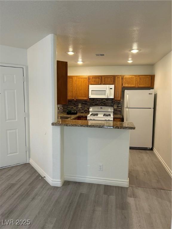 5044 S Rainbow Blvd Unit 106, Las Vegas, NV 89118 - kitchen featuring dark stone counters, wood finished floors, brown cabinetry, white appliances, and baseboards